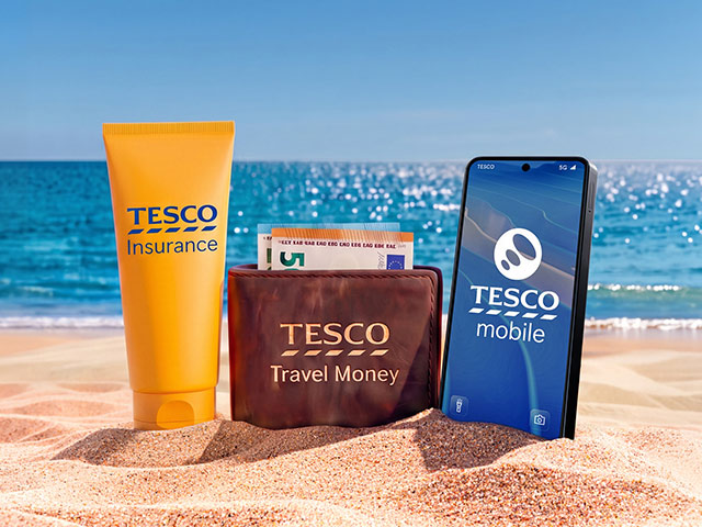 Sunscreen, wallet and phone featuring Tesco Insurance, Tesco Travel Money and Tesco Mobile logos, in the sand beside the sea.
