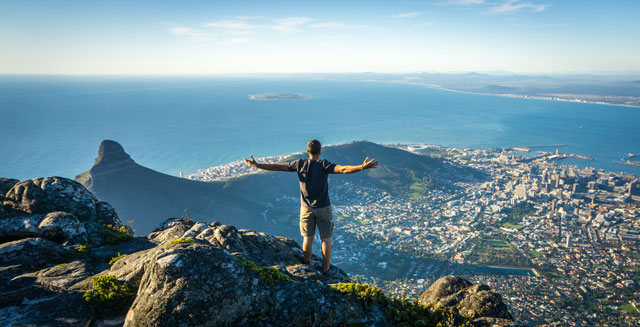 Man standing on a mountain looking over city.